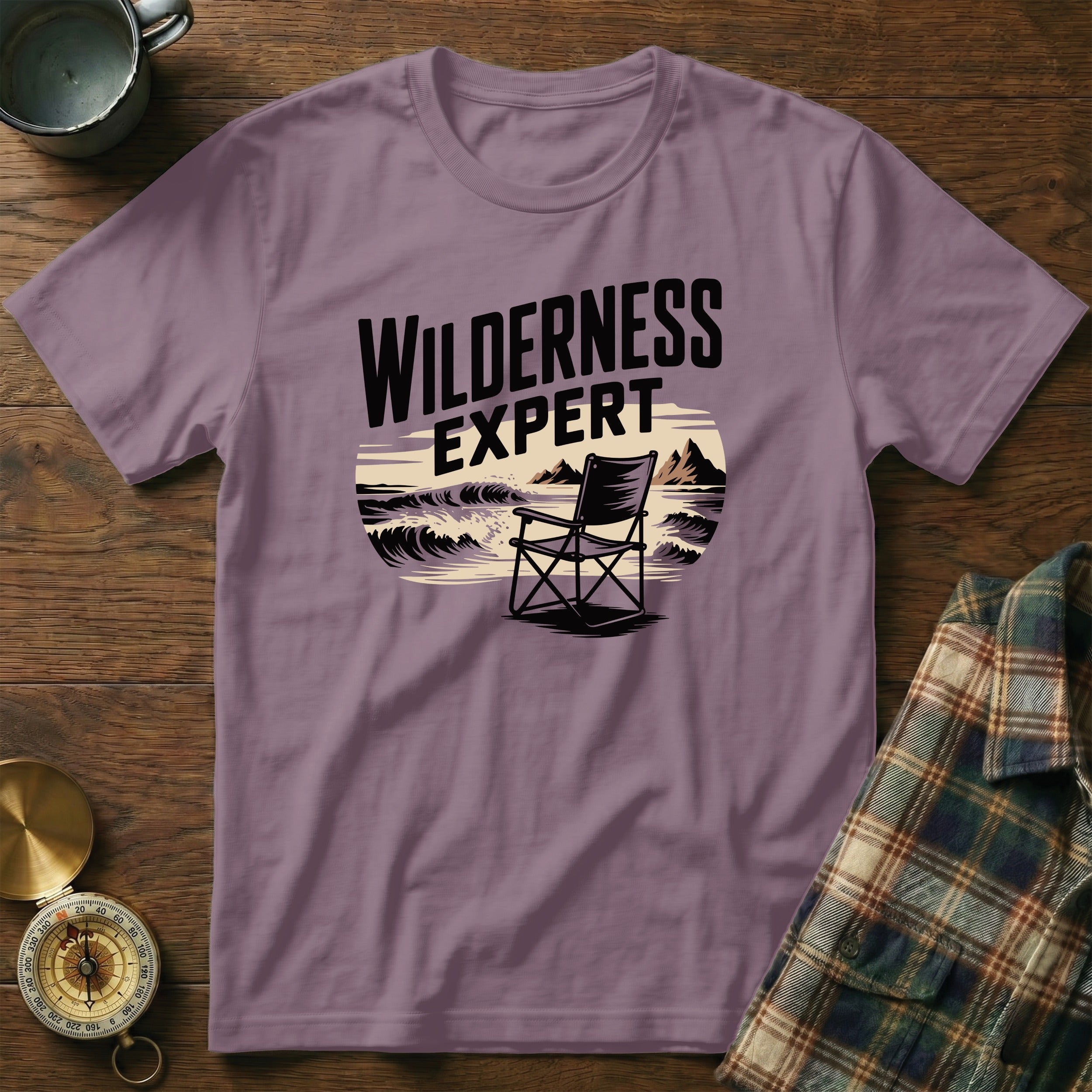 Purple t-shirt with "Wilderness Expert" text and camping chair on beach graphic.