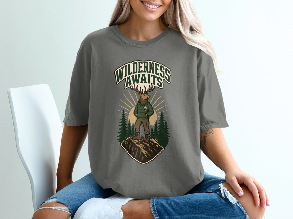 T-shirt graphic with text "WILDERNESS AWAITS," elk, and evergreen trees.