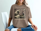 T-shirt graphic featuring a wave, UFO, and text "The Unexplained Tide".
