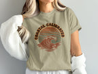 T-shirt with "Coastal Calibrated" text and a stylized wave and palm trees graphic.