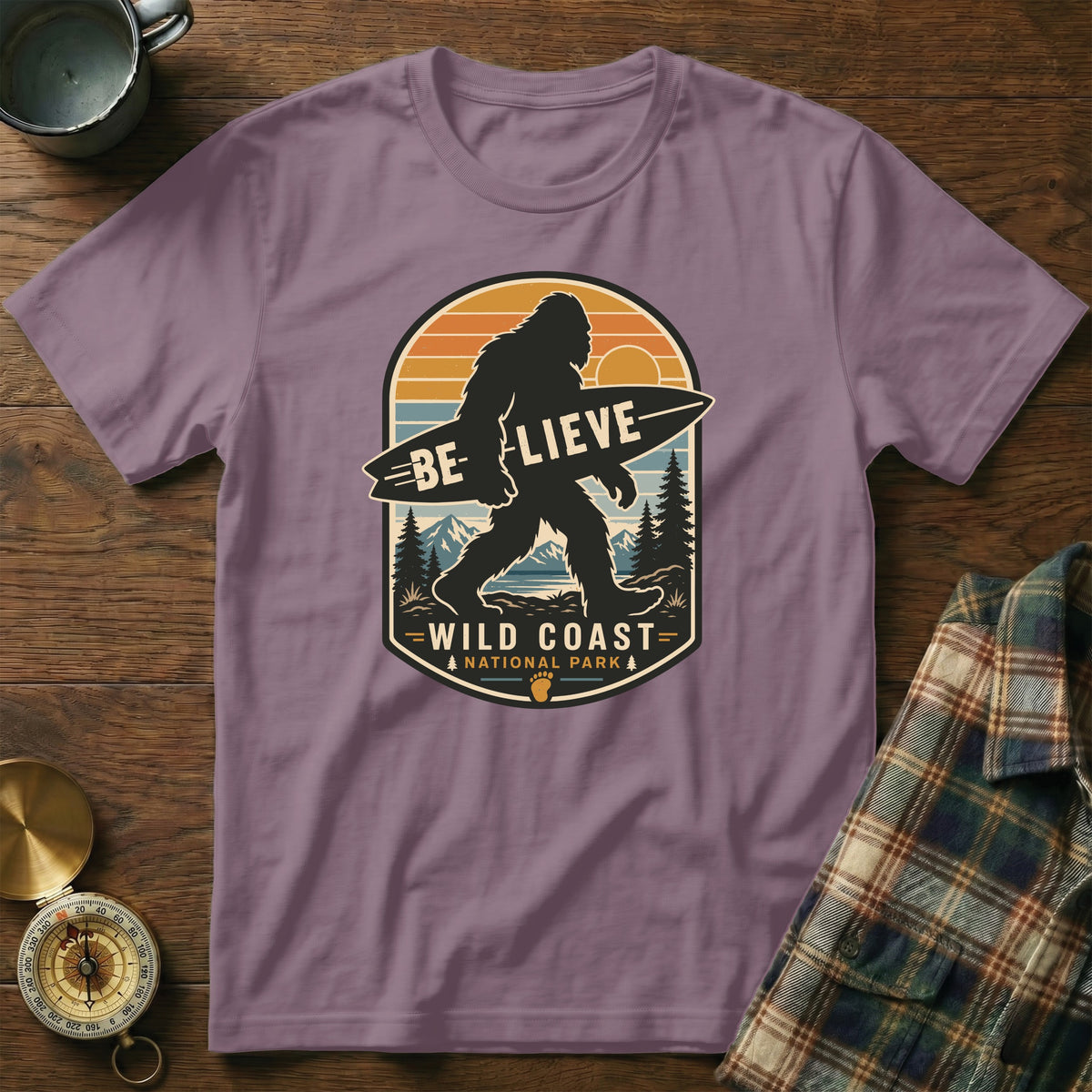 Purple t-shirt with Bigfoot carrying surfboard graphic, "Believe Wild Coast National Park" text.