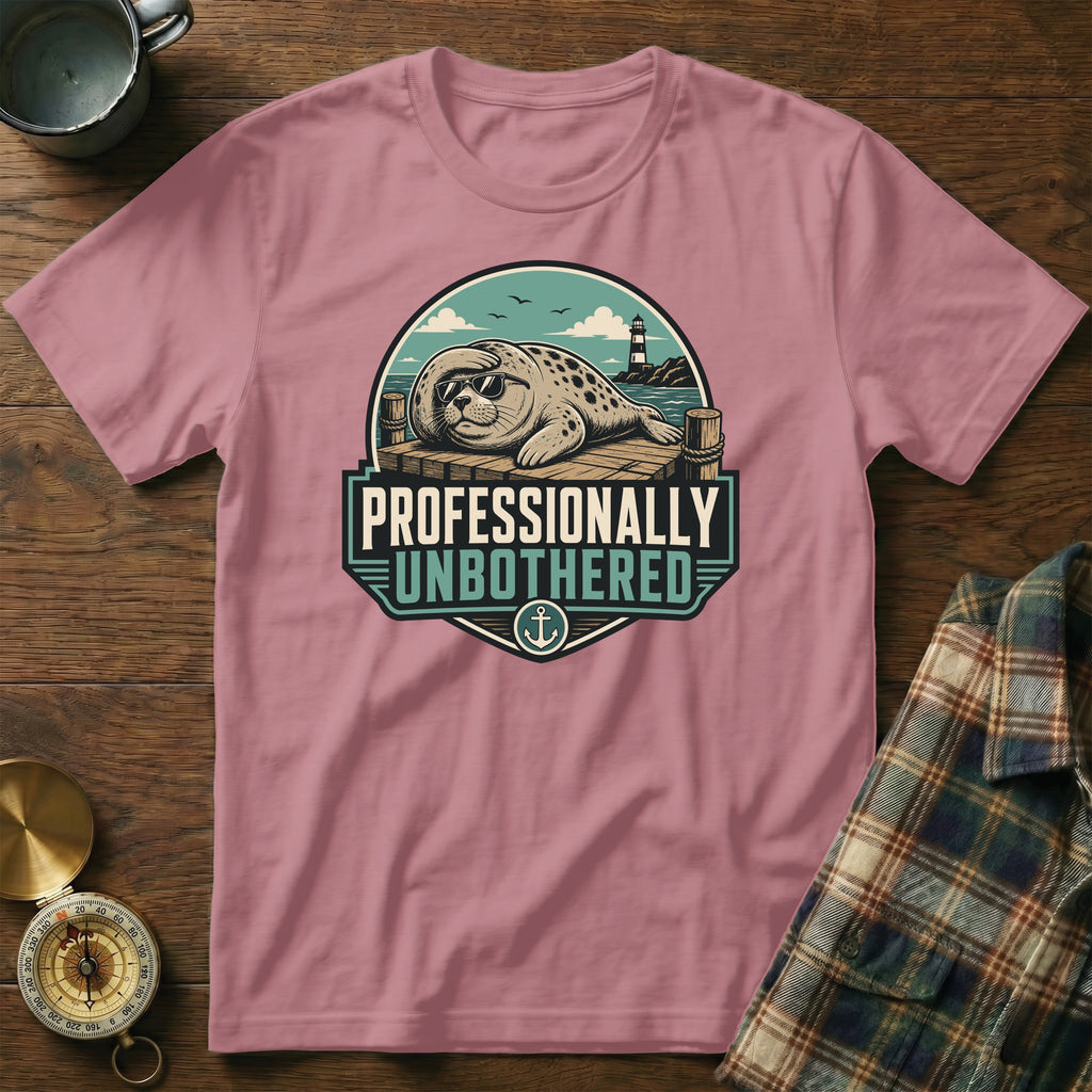 Pink t-shirt with a graphic of a seal in sunglasses on a dock, reading "Professionally Unbothered".
