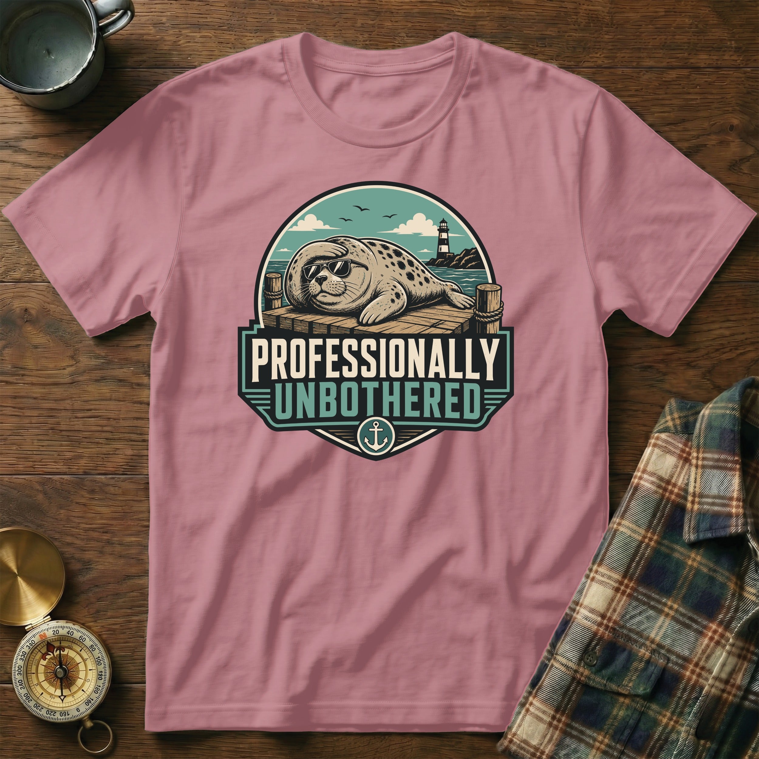 Pink t-shirt with a graphic of a seal in sunglasses on a dock, reading "Professionally Unbothered".