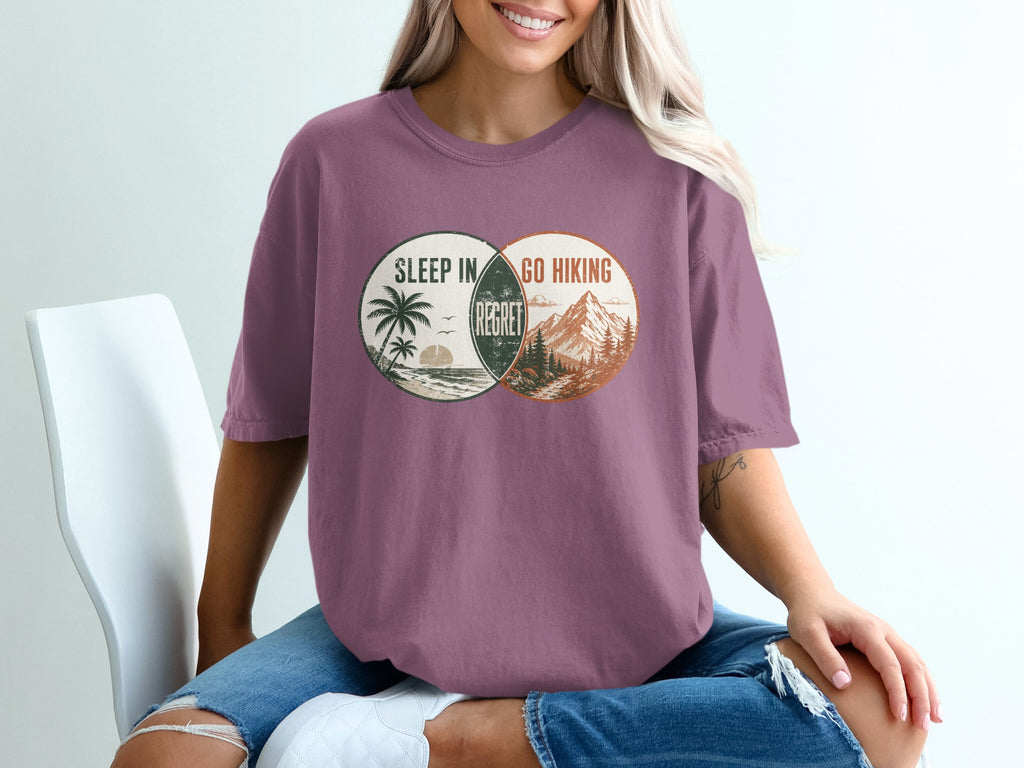 T-shirt graphic with overlapping circles: beach scene and mountains, text "Sleep In", "Go Hiking", "Regret".