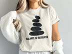 T-shirt with stacked stones graphic and "BALANCE IS OVERRATED" text.