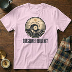 Pink t-shirt with a circular logo featuring a wave, sun, bird, and the text COASTLINE FREQUENCY.