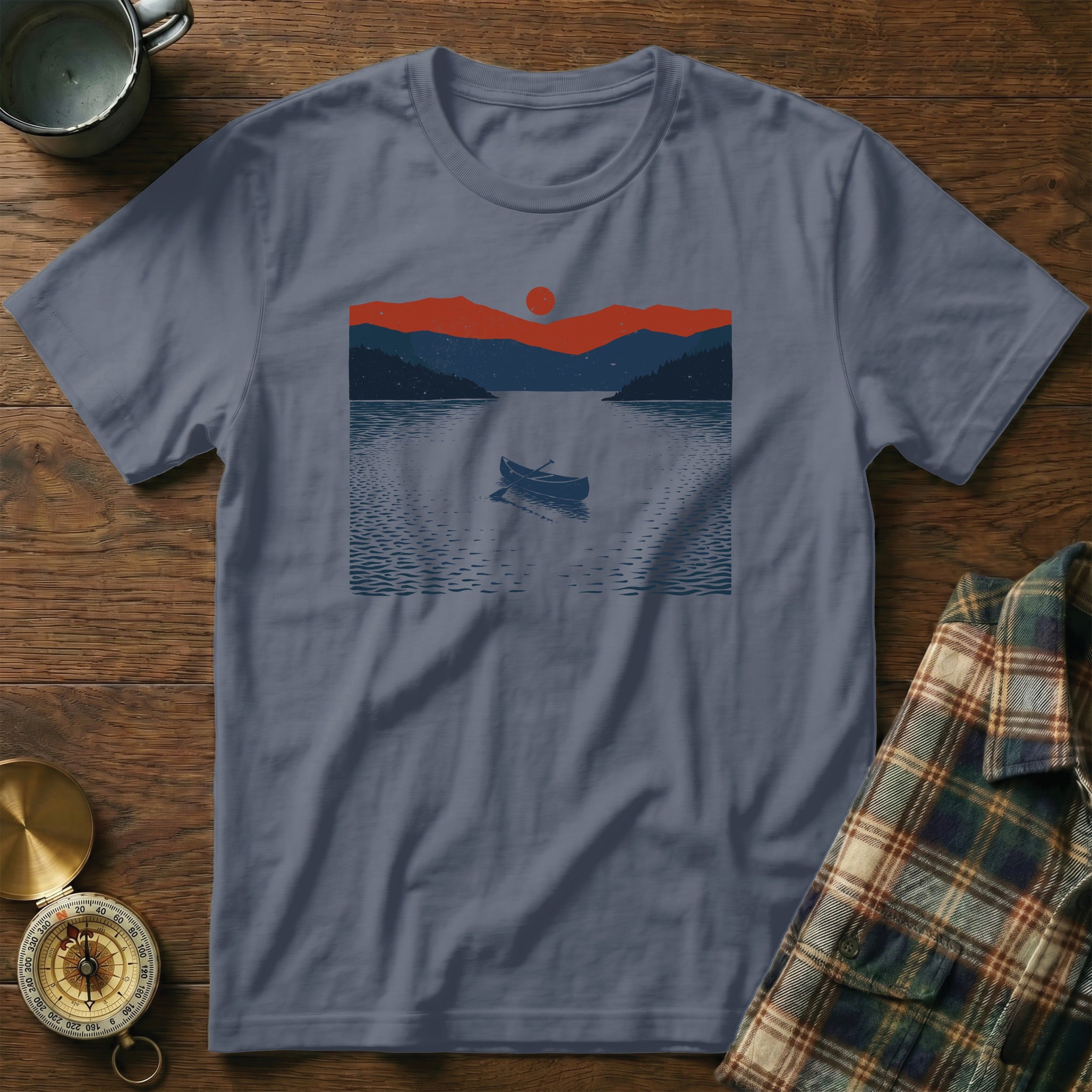 T-shirt with a graphic of a rowboat on a lake with mountains and a sunset.