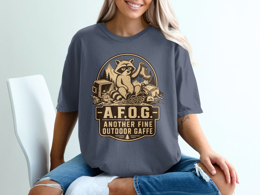 T-shirt graphic with raccoon, boot, camping gear, and text "A.F.O.G. Another Fine Outdoor Gaff".