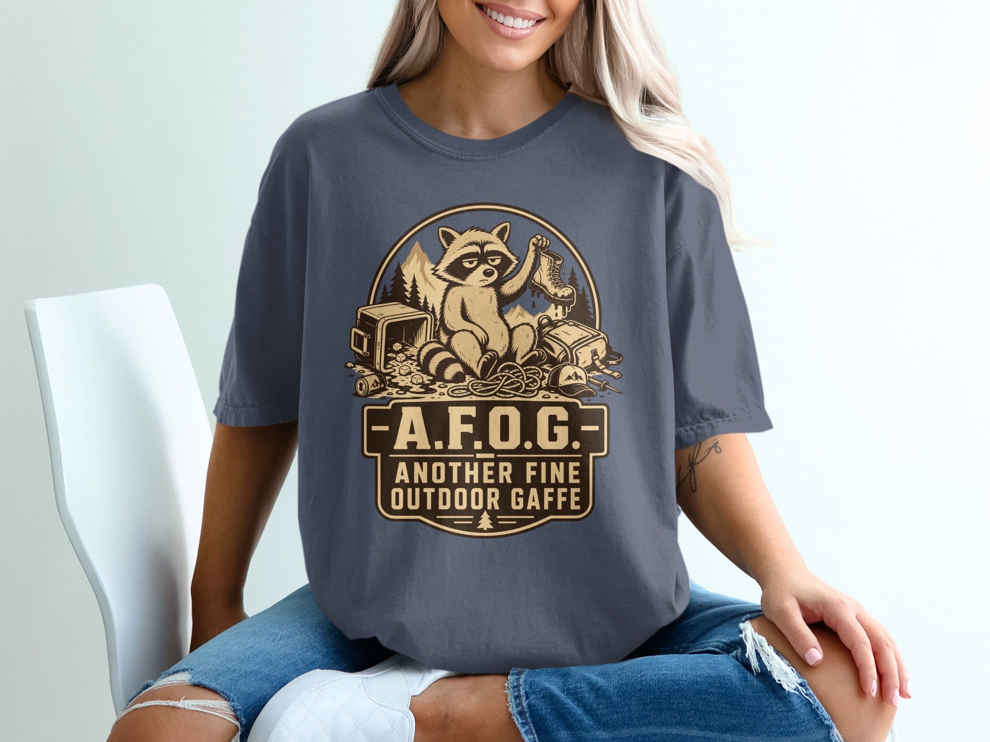 T-shirt graphic with raccoon, boot, camping gear, and text "A.F.O.G. Another Fine Outdoor Gaff".