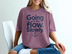 A person wears a mauve t-shirt with navy text reading Going with the flow. Slowly. and an anchor graphic.