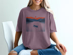 T-shirt with graphic of a canoe on a lake during sunset with mountains.