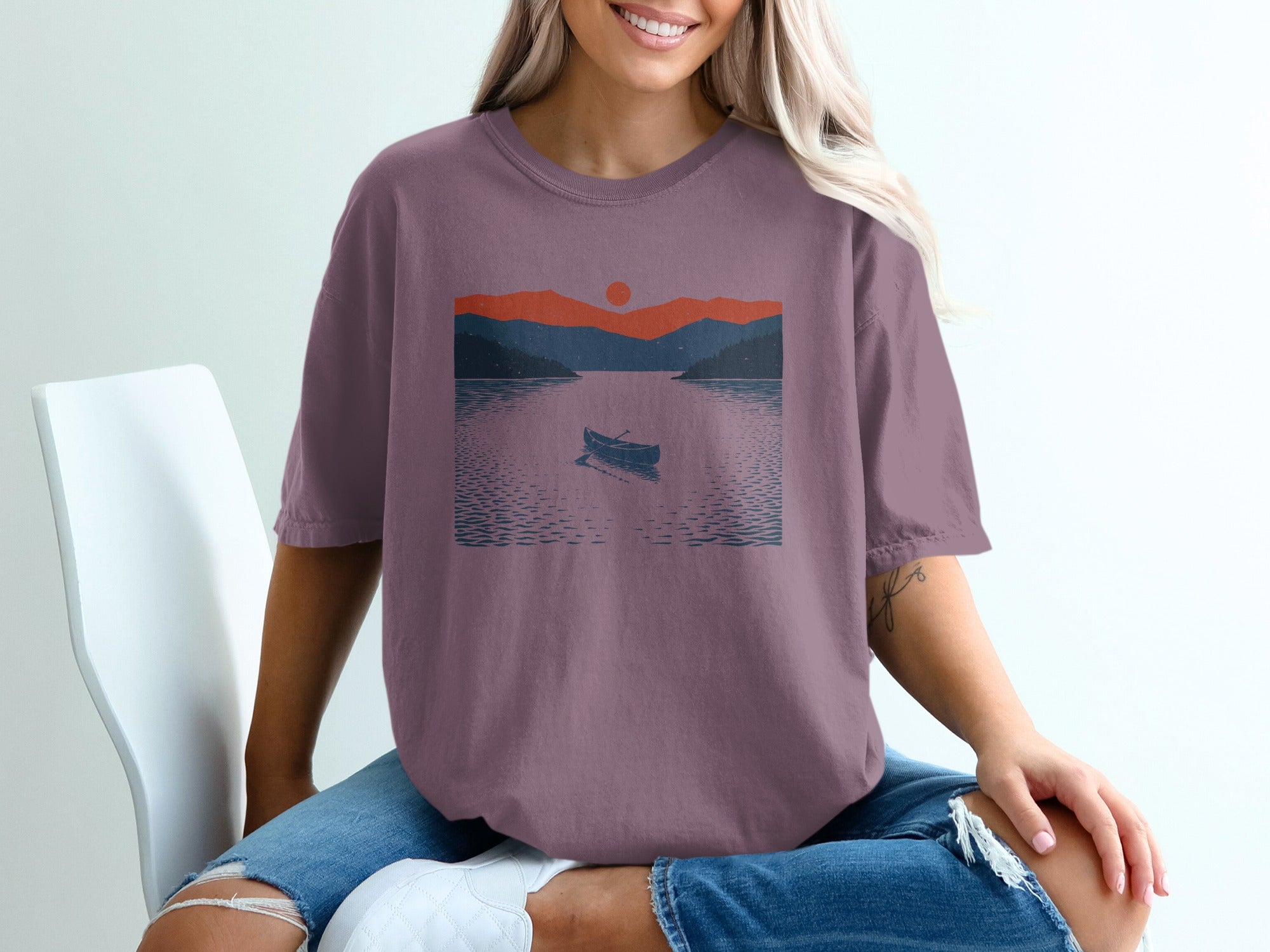 T-shirt with graphic of a canoe on a lake during sunset with mountains.