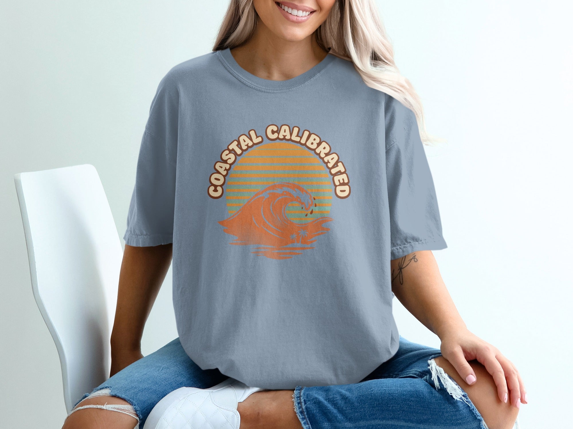 Grey t-shirt with "Coastal Calibrated" text and a sunset wave graphic.
