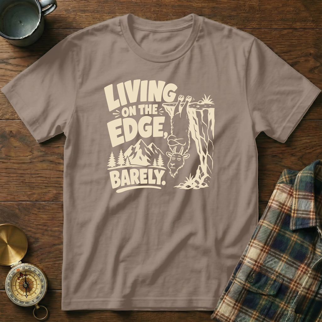 T-shirt with text "Living on the edge, barely" and a goat hanging from a cliff.