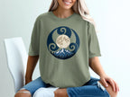 Green t-shirt with a circular graphic featuring mountains, trees, and a moon.