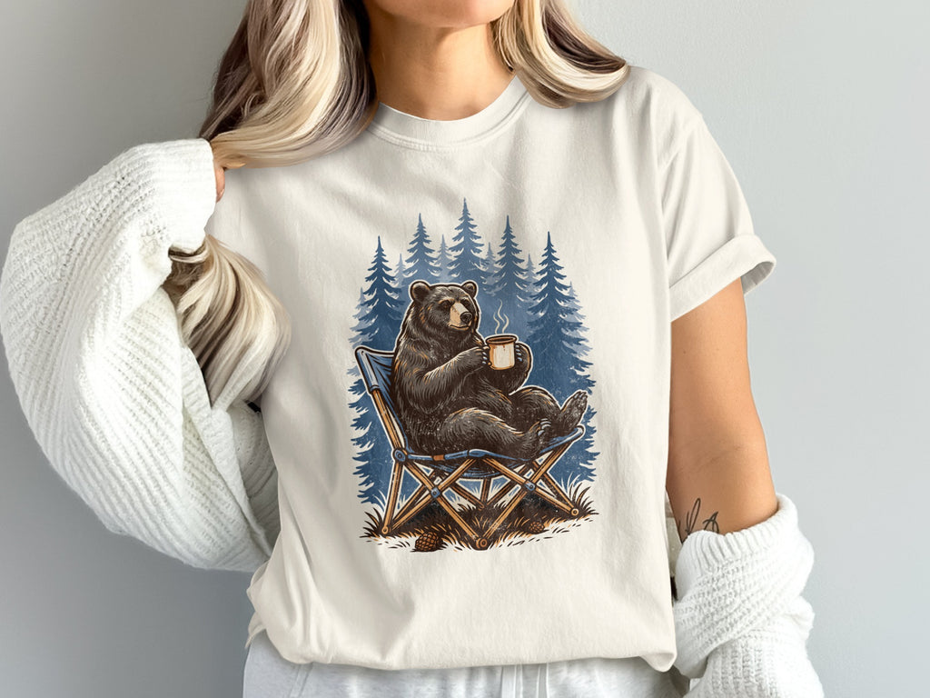 Bear sitting in a camping chair holding a coffee mug with trees behind it.