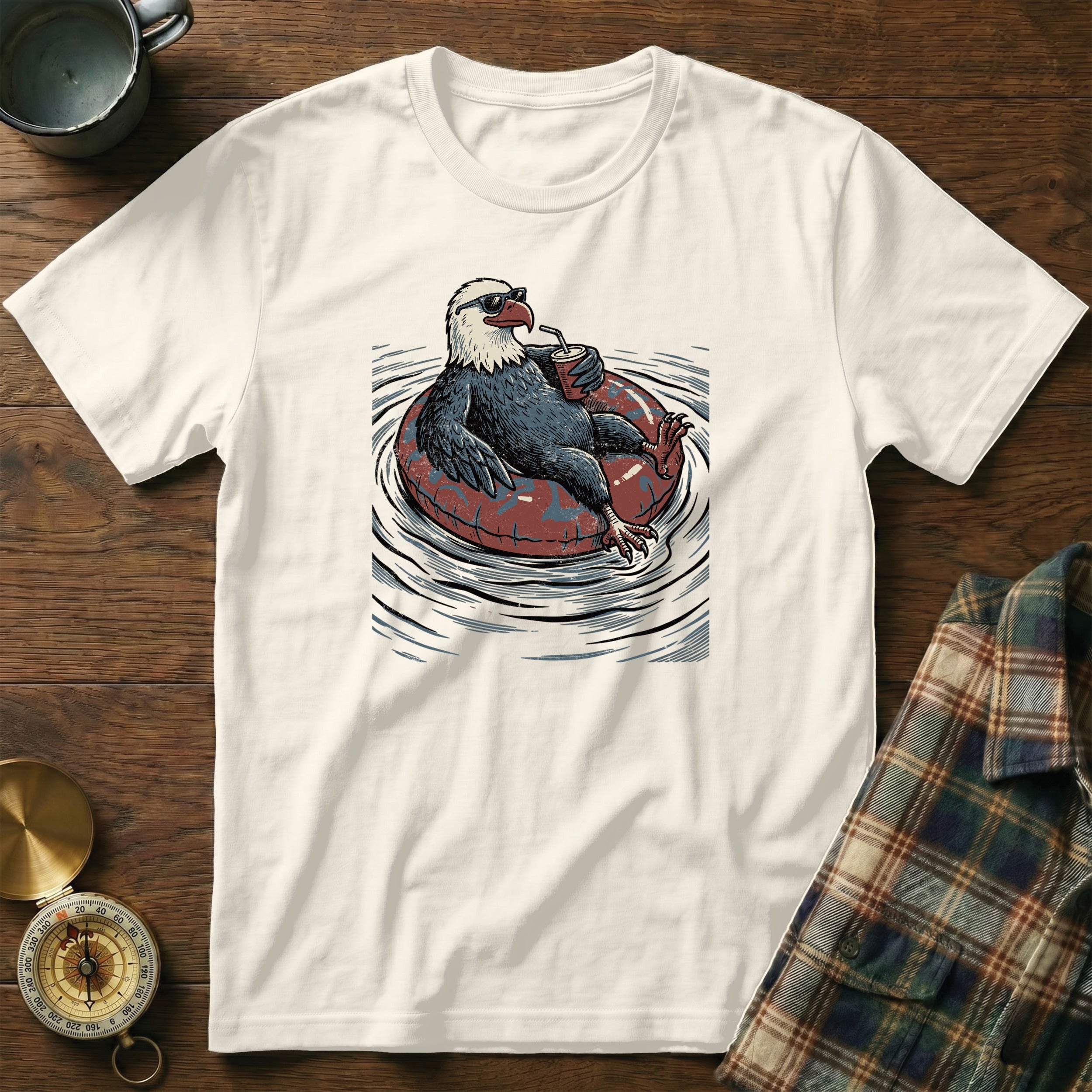 T-shirt features a graphic of a bald eagle wearing sunglasses on an inner tube with a drink.