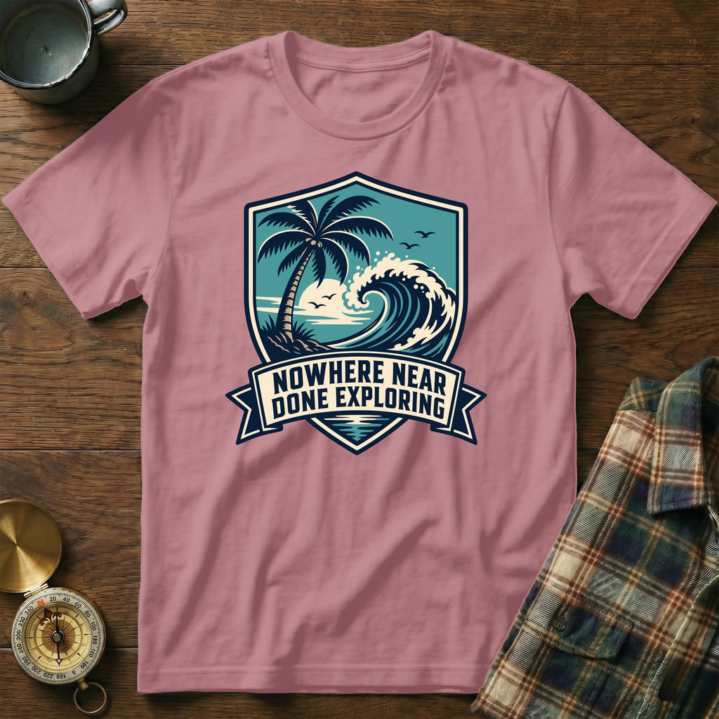 T-shirt with a shield graphic featuring a palm tree, wave, and quote "Nowhere Near Done Exploring".