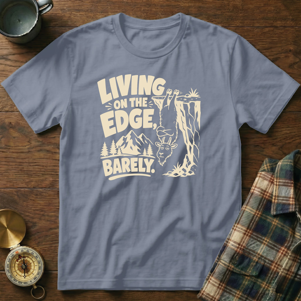 T-shirt with a goat hanging from a cliff and text "LIVING ON THE EDGE, BARELY."