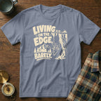 T-shirt with a goat hanging from a cliff and text "LIVING ON THE EDGE, BARELY."