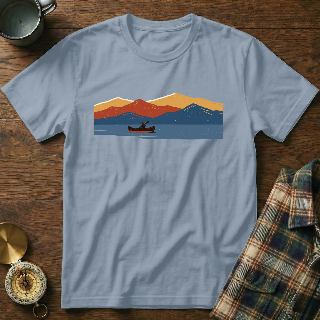 Light blue t-shirt with a minimalist graphic of a person in a canoe on a lake with mountains.