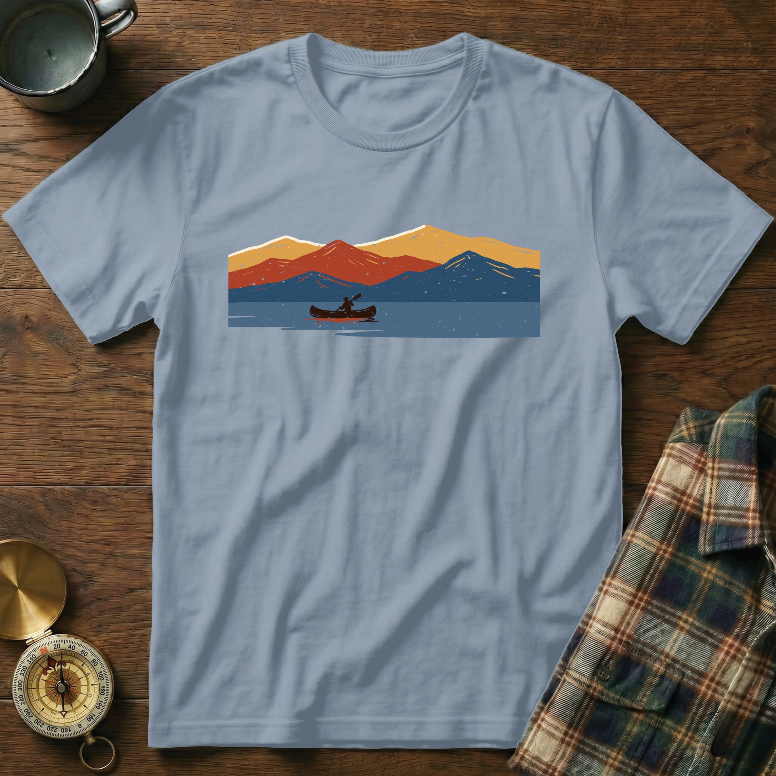 Light blue t-shirt with a minimalist graphic of a person in a canoe on a lake with mountains.