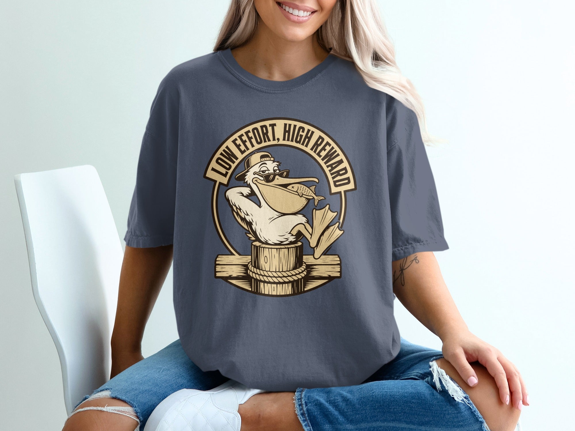 T-shirt with a cartoon pelican wearing sunglasses and a hat, holding a fish, with text "LOW EFFORT, HIGH REWARD".