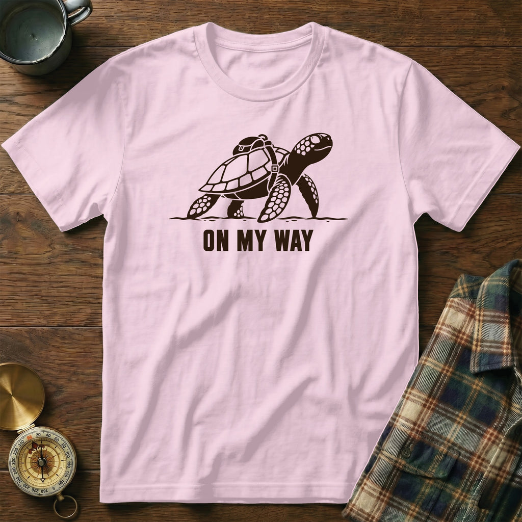 Pink t-shirt with a graphic of a turtle wearing a backpack and the text "ON MY WAY".