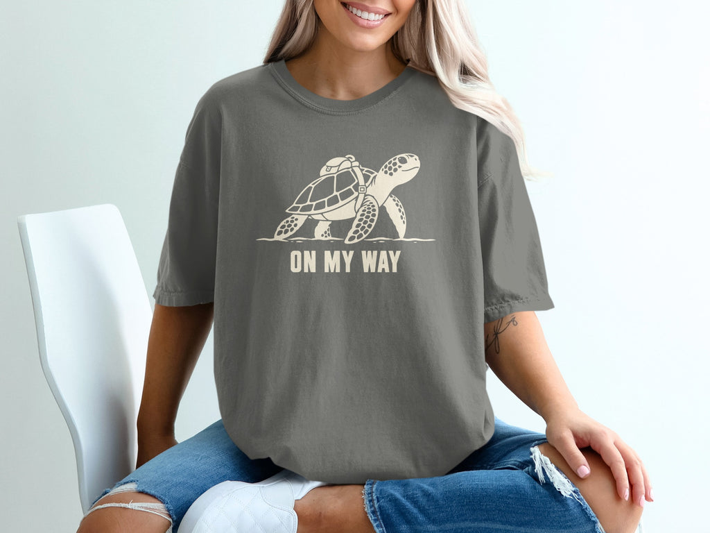 Grey t-shirt with a cream graphic of a turtle carrying a backpack, captioned "ON MY WAY".