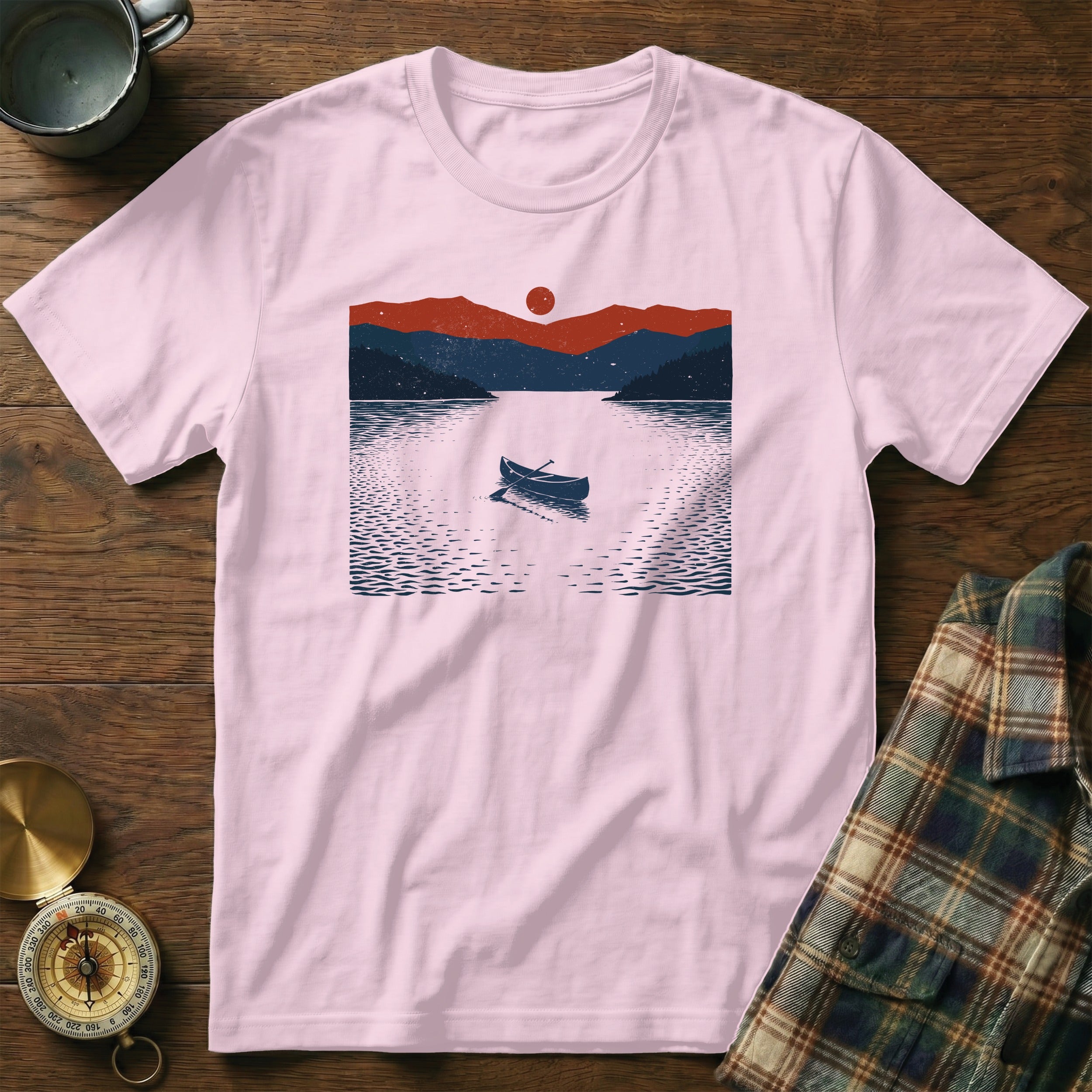 Pink t-shirt with a lake, mountains, sun, and canoe graphic.