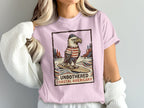 Eagle in striped shirt surfing under text "UNBOTHERED COASTAL AMERICANA".