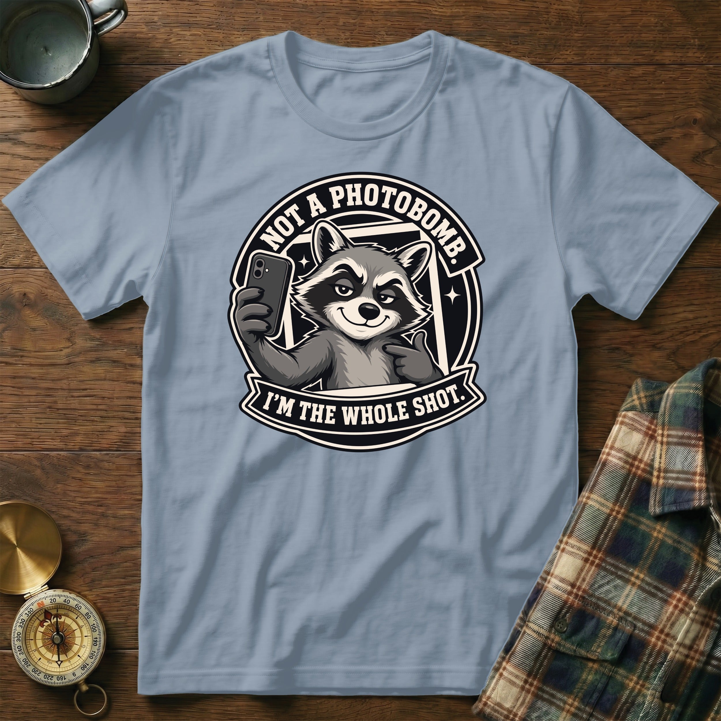 Light blue t-shirt featuring a raccoon taking a selfie with text "Not a photobomb. I'm the whole shot."