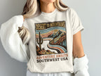 T-shirt with desert mountains landscape and text "DESERT TO MOUNTAINS ADVENTURE AWAITS SOUTHWEST USA".