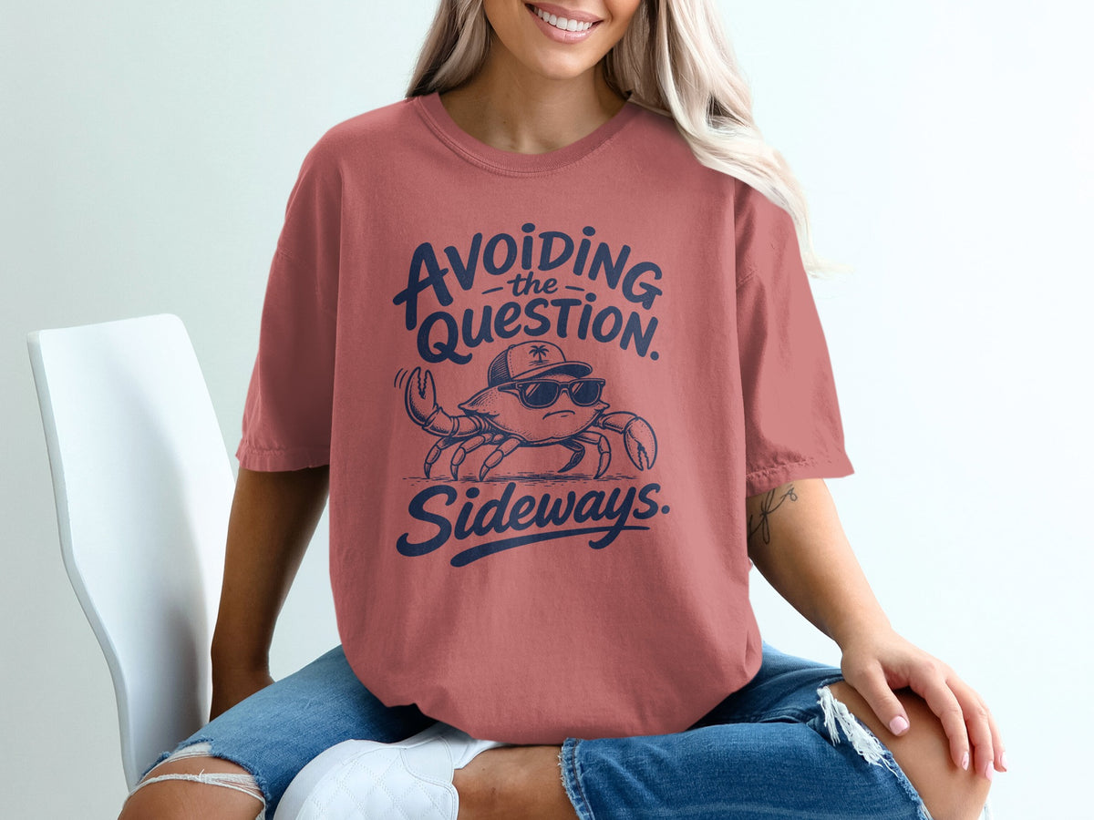 A person wearing a dusty pink t-shirt with a blue graphic of a crab wearing sunglasses and a cap, accompanied by the text "Avoiding the Question Sideways."