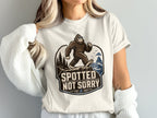 Bigfoot wearing sunglasses walks on a cliff with "Spotted Not Sorry" text.