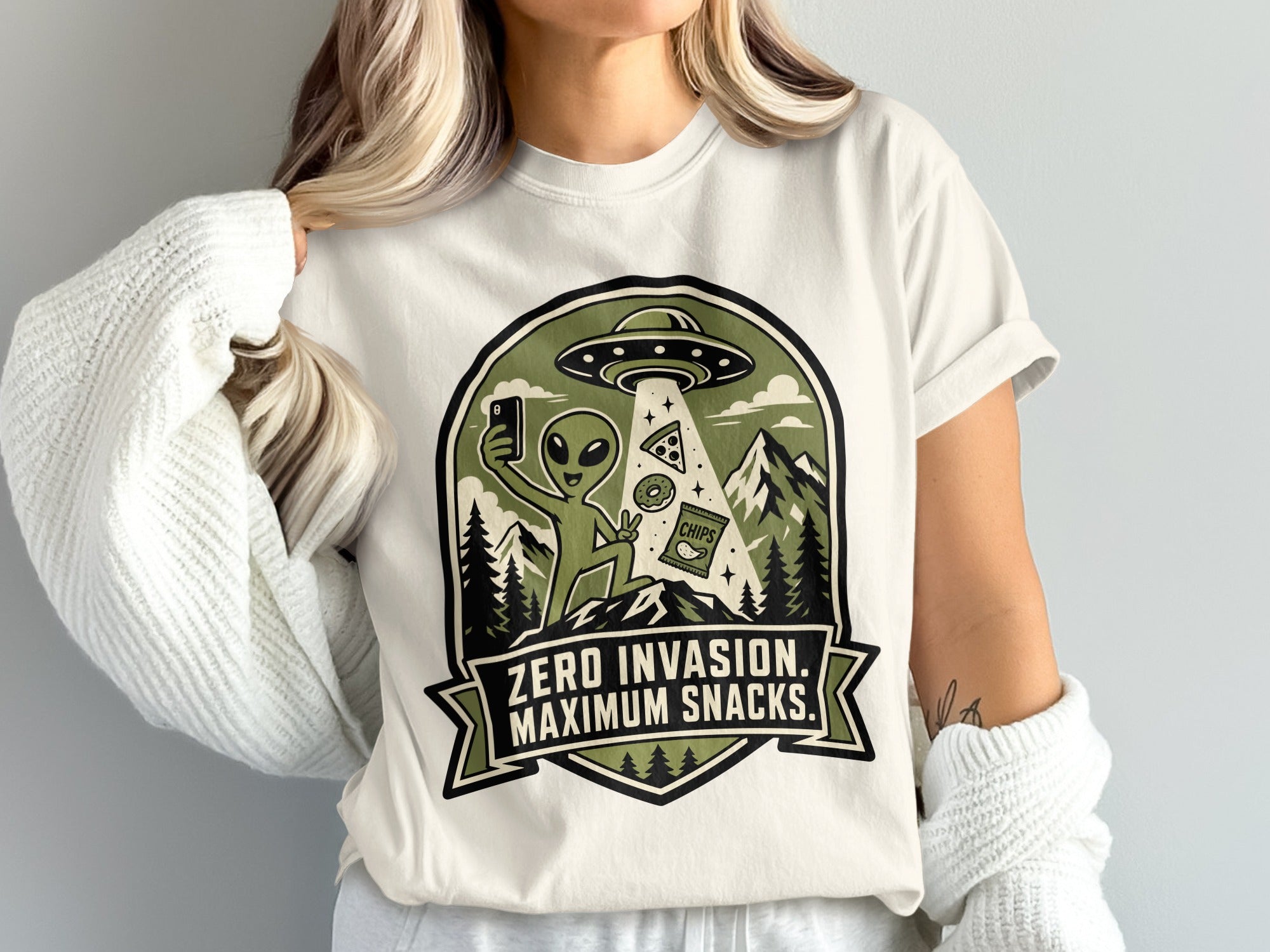 Alien taking a selfie with pizza, donuts, and chips under UFO. "Zero Invasion. Maximum Snacks."