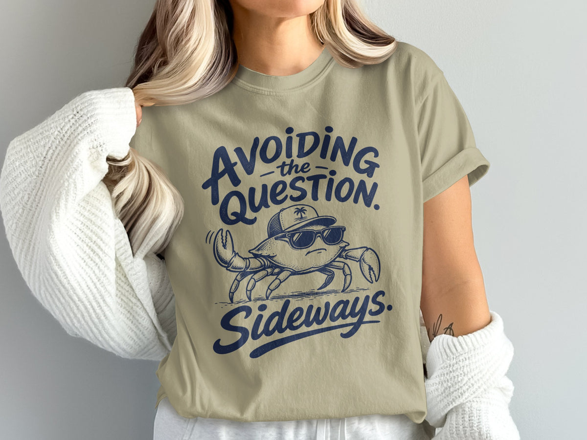 A person wears a beige t-shirt featuring a blue illustration of a crab wearing sunglasses and a cap, accompanied by the text Avoiding the question sideways.