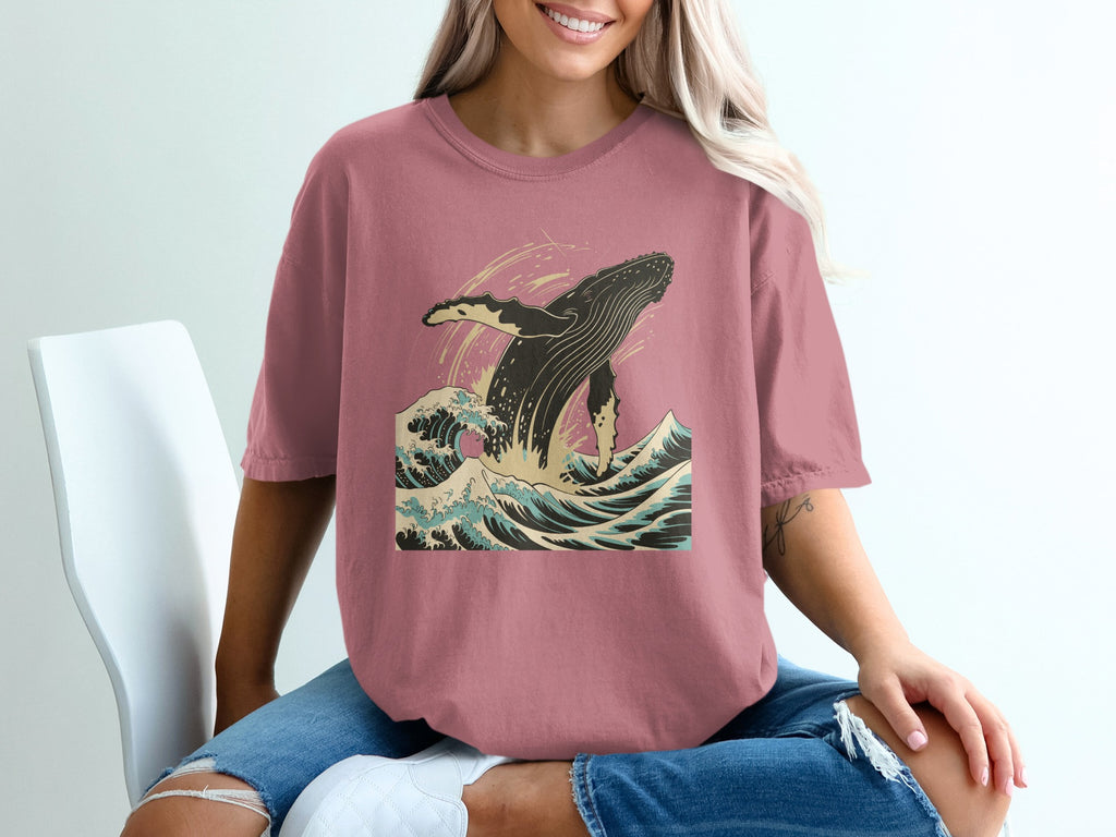 Pink t-shirt with a jumping whale in ocean waves graphic.