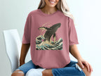 Pink t-shirt with a jumping whale in ocean waves graphic.