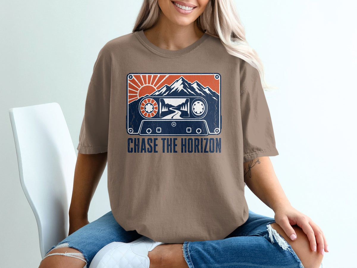 T-shirt with vintage cassette tape graphic featuring mountains, sun, and road, text reads "CHASE THE HORIZON".