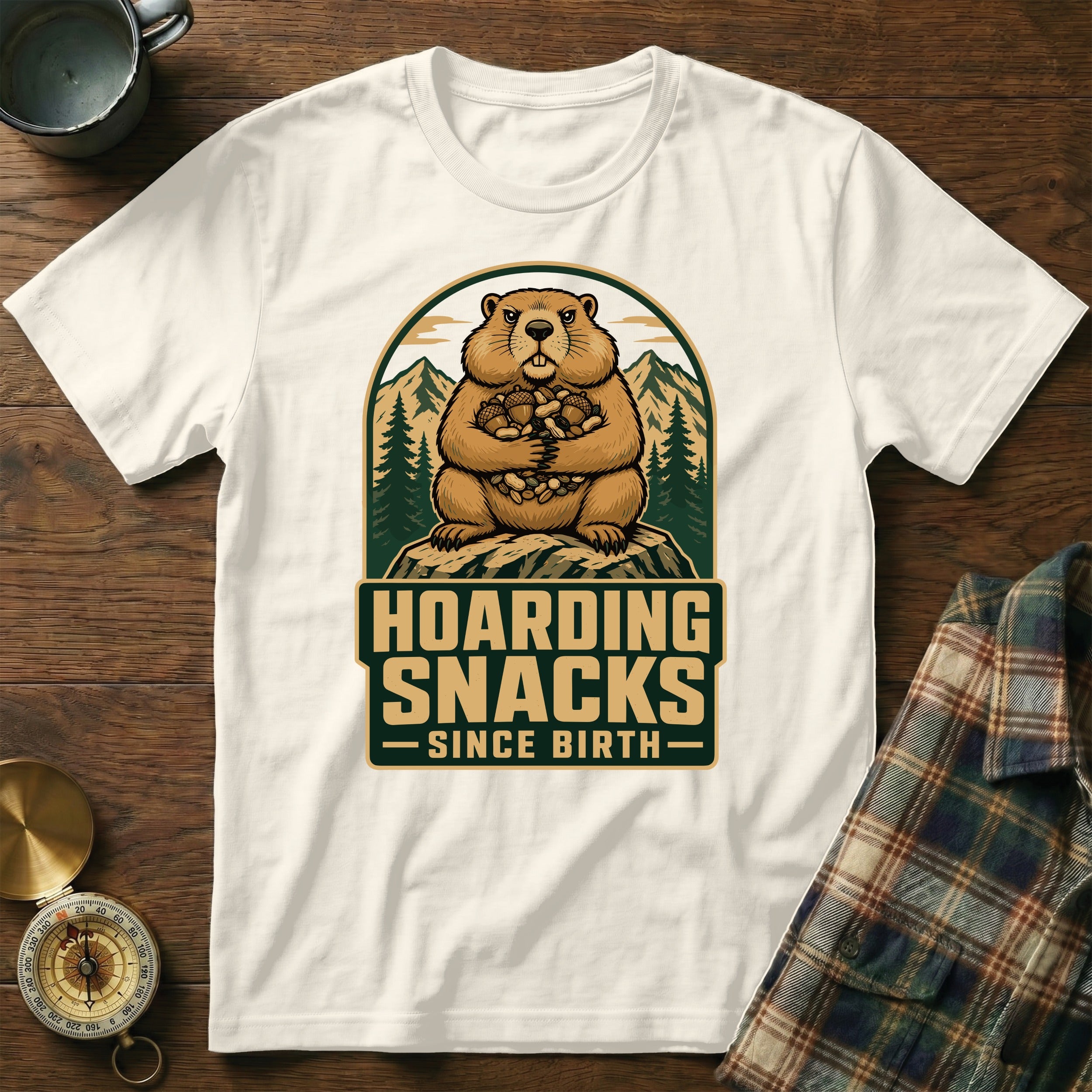 White t-shirt with a graphic of a groundhog hoarding nuts, with text "Hoarding Snacks Since Birth".