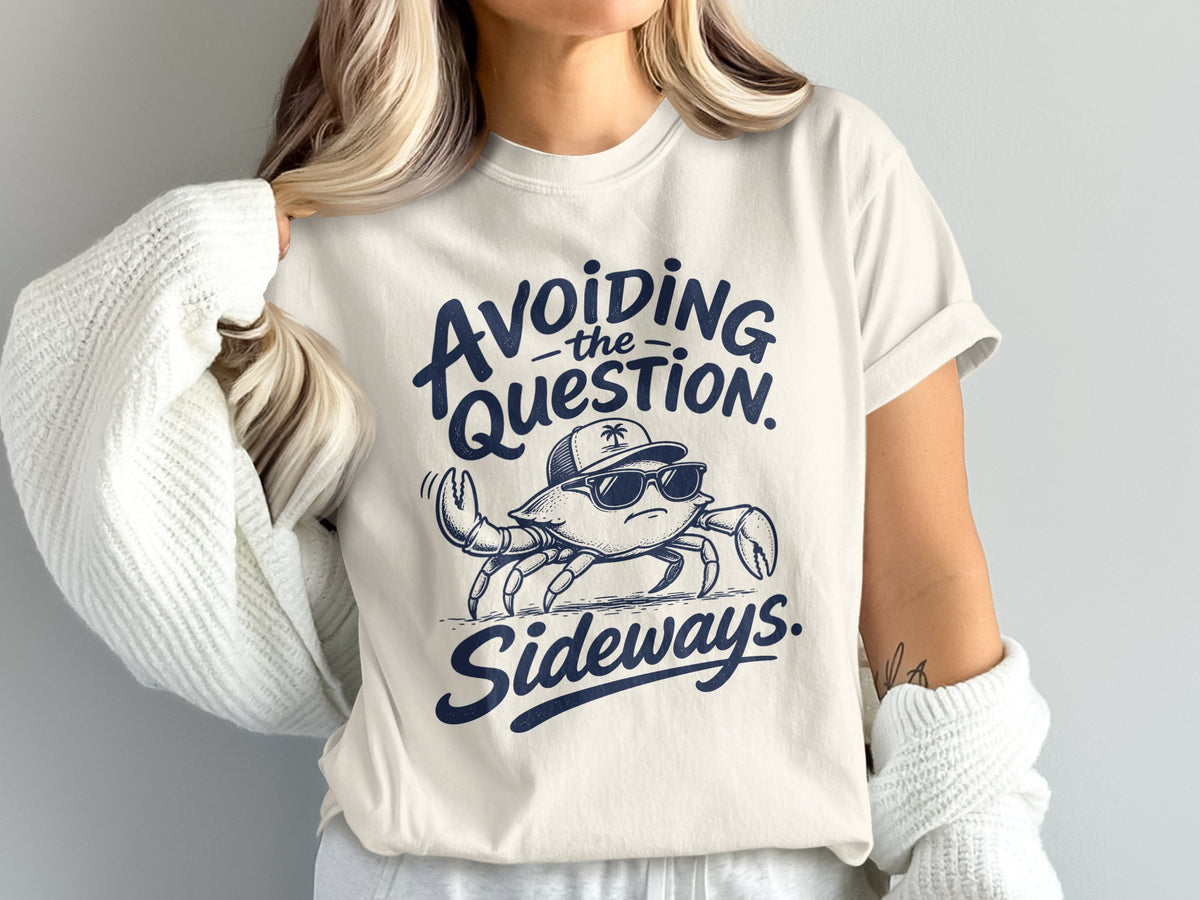A woman wearing a cream t-shirt featuring a graphic of a crab wearing sunglasses and a cap, with the text Avoiding the question sideways.