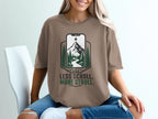 Brown t-shirt with graphic of phone showing mountains, trees, and river, "Less Scroll. More Stroll."