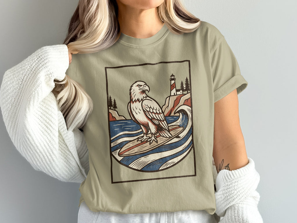 T-shirt with illustration of an eagle surfing by a lighthouse and trees.