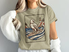 T-shirt with illustration of an eagle surfing by a lighthouse and trees.