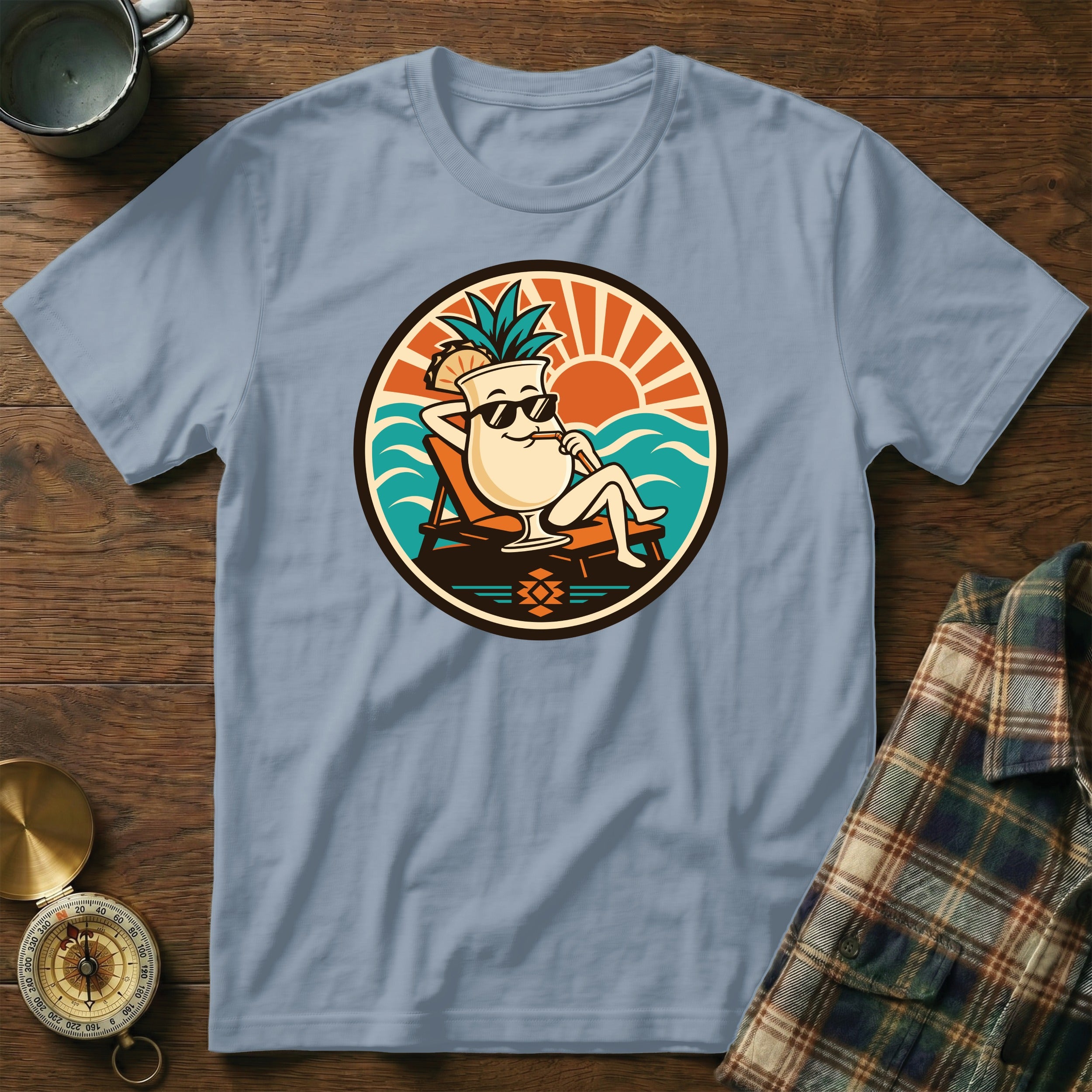 T-shirt graphic of a cartoon cocktail with pineapple on a lounge chair at the beach.