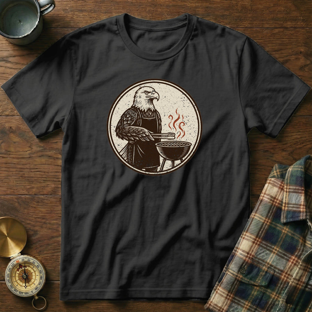 Black t-shirt with eagle grilling on a circular graphic, laid on a wooden surface.