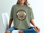Olive green t-shirt with "Survived an Adult Conversation" text and badge graphic.
