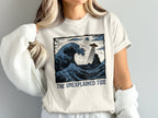 T-shirt with blue wave, UFO, lighthouse, and "The Unexplained Tide" text.