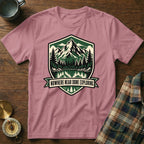 Pink t-shirt with a shield logo featuring mountains, trees, and the text "Nowhere Near Done Exploring".